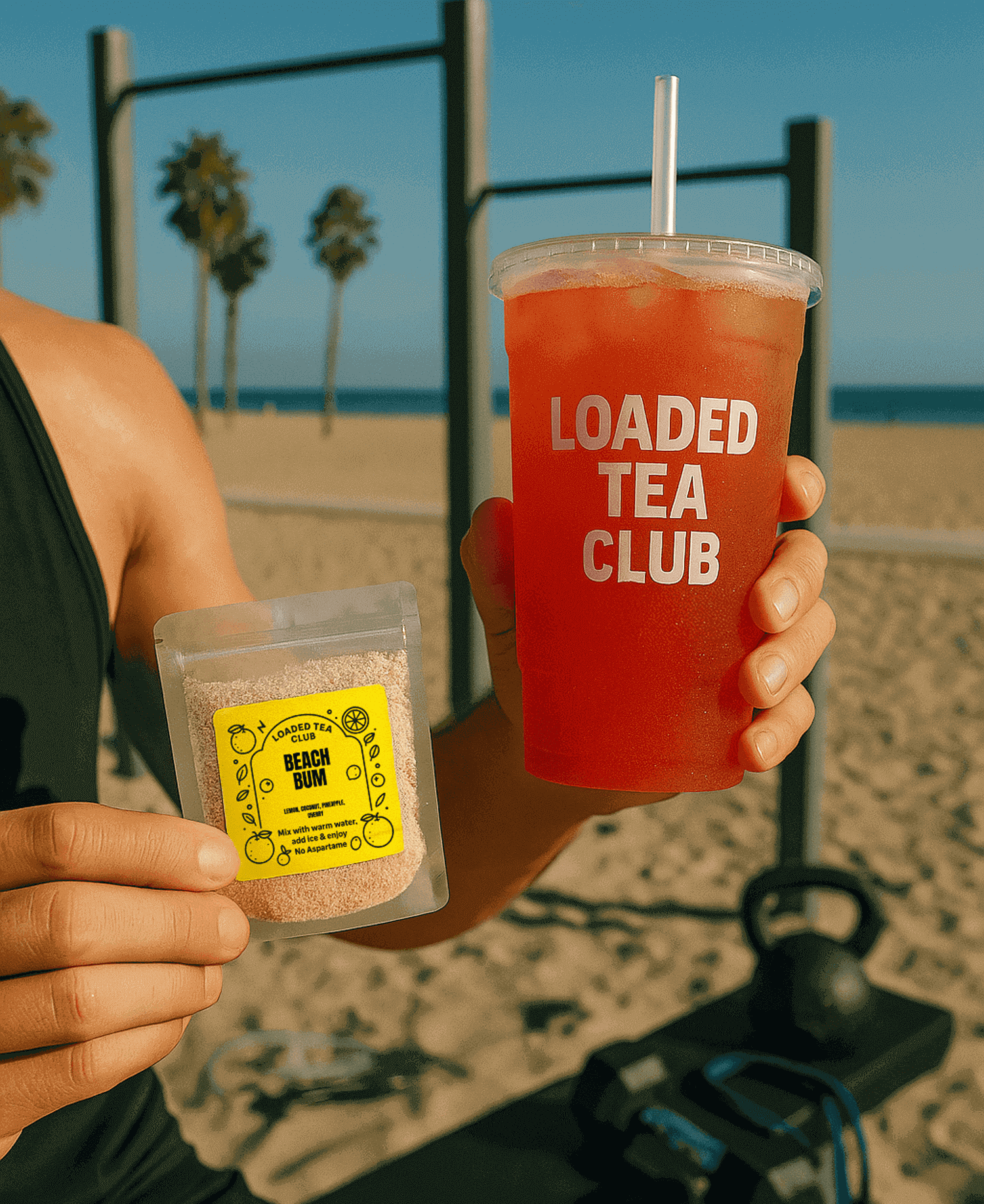 A person holds a packet of loaded tea mix and a refreshing loaded tea drink at the beach.